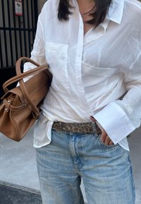 Witte linnen shirt met lange mouwen, lichtgewassen denim jeans en een bruine leren handtas met contrasterende stiksels en een luipaardprint riem.