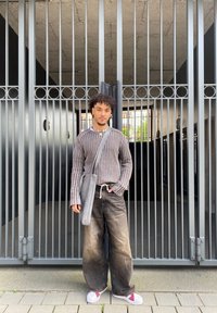 Grey vertically striped sweater, loose dark jeans, white shoes with red accents, grey shoulder bag, standing against a metal gate.