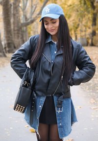 Melna ādas džakete motociklistam, pārklāta ar džinsa kreklu, ar zilu cepuri un melnu rokassomiņu ar naglām. Apģērbs ietver melnu svārku un zeķubikses.