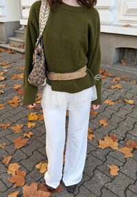 Oliwkowy, oversize sweter, beżowy pasek, biały warstwowy tiul, szerokie białe spodnie i brązowe buty na tle opadłych liści.