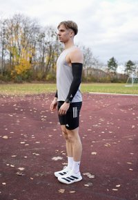 Mustad spordikäevarrukas, hall tanktop, mustad lühikesed püksid valgete triipudega ja valged tossud mustade detailidega. Välitreki keskkond.