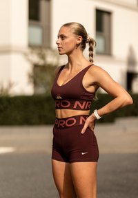 Kestenasti atletski crop top i kratke hlače s kontrastnim brendingom. Glatka, prilagođena tkanina; Nike logo na hlačama; detalj u obliku ključa na gornjem dijelu.