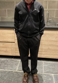 Jacket fleece negru cu fermoar peste un polo vișiniu, asortat cu pantaloni negri și pantofi maro. Design simplu și discret, potrivit pentru ținute casual.