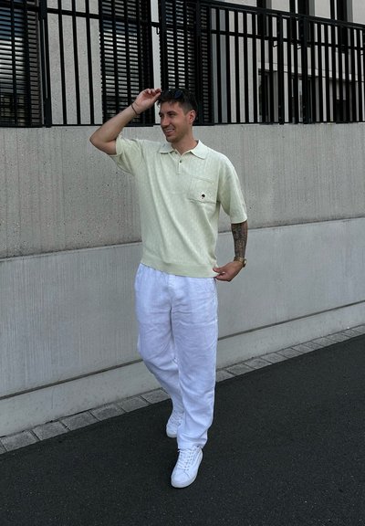 Polo shirt texturizado verde claro de mangas cortas, con un bolsillo en el pecho. Combinado con pantalones de lino blanco sueltos y zapatillas blancas.