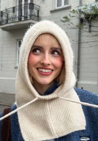 Cappuccio lavorato a maglia color crema con coulisse, texture a coste e vestibilità ampia. Indossato sopra una giacca in pile blu navy, con un aspetto morbido e accogliente.