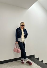 Μπλε τζάκετ τζην πάνω από λευκό ριγωτό μπλουζάκι, σκούρες τζιν με διπλωμένα μπατζάκια, ροζ τσάντα και μπορντό αθλητικά παπούτσια. Λιτές μαύρες ηλιόκαρδες γυαλιά.