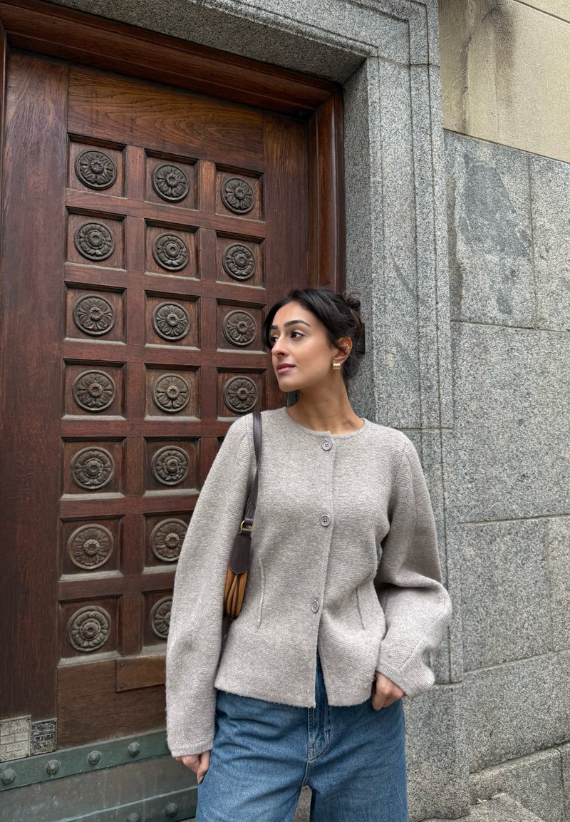 Hellgraue Strickjacke aus Wollmischung mit rundem Ausschnitt, Knopfleiste vorne und überschnittenen Schultern, kombiniert mit hoch taillierten Jeans.