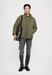 Casaco acolchoado verde com gola alta, camisa xadrez cinza por baixo, jeans cinza e bolsa de ombro em couro preto, além de sapatos pretos.