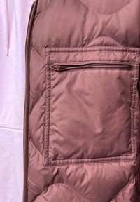 Duvet prsluk u mauve boji, s patentnim zatvaračem na prednjoj strani. Materijal izgleda glatko s mat završnom obradom i suptilnim sjajem.