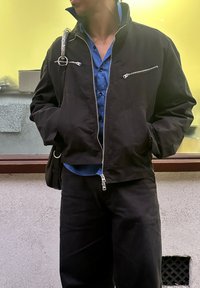 Mustast lõhestatud jakk hõbedaste tõmblukkudega, kandes selle all sinist särki; kombineeritud tumedate pükstega. Aksessuaarina on õlakott.