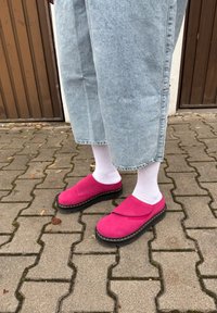 Felle roze suède instappers met een zwarte plateauzool, gedragen met witte sokken, gecombineerd met lichtblauwe denim culottes op een stenen straat.