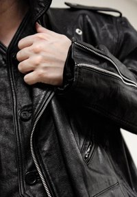 Veste en cuir noir avec fermeture éclair à l'avant et boutons-pression, finition texturée et détails subtils de coutures sur les manches.