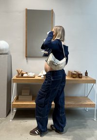 Navyblauwe oversized broek en een geribbeld donker sweater gecombineerd met een crèmekleurige schoudertas. Eenvoudige houten plank met decoratieve items en verpakkingen.