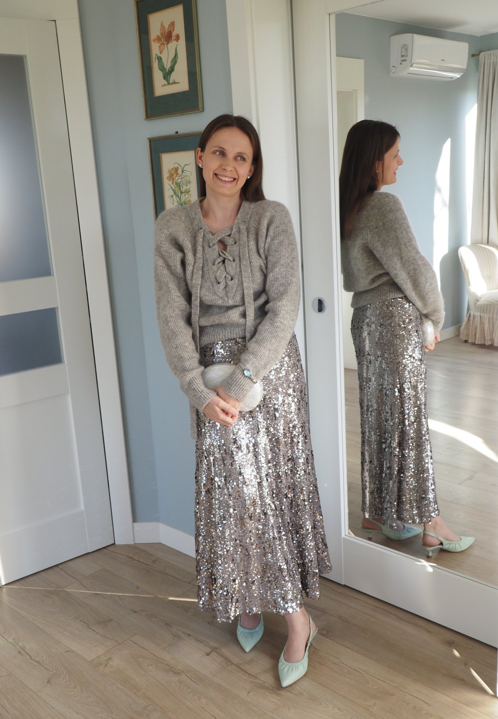 Grå strikket genser med snøring, kombinert med et langt, glitrende sølvskjørt med paljetter. Lysegrønne spisse hæler og en gjennomsiktig clutch.