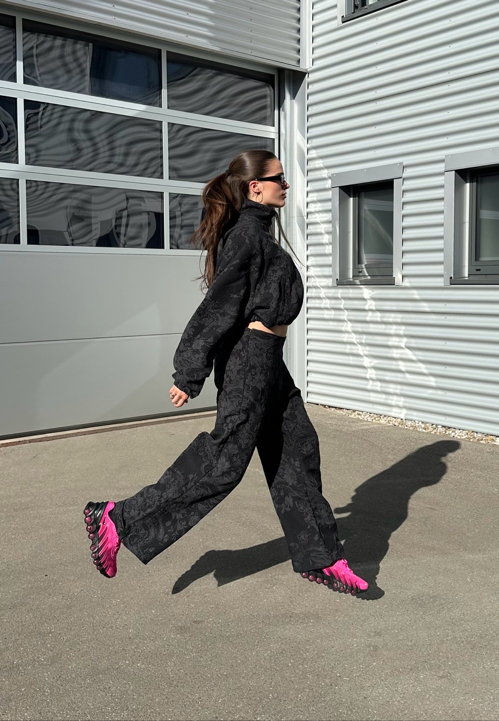 Sweatshirt oversized com padrão floral preto e calças largas combinando, acompanhados de sapatos rosa brilhante com sola texturizada, em movimento.