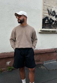 Beige gebreide trui met een ronde hals, gecombineerd met zwarte op maat gemaakte short. De persoon draagt een witte pet en witte sokken. Eenvoudig ontwerp.