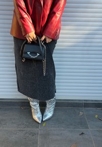 Blazer di pelle rossa, gonna nera con texture, borsa nera con catena d'argento e stivaletti argento lucidi con punta a punta. Sfondo uniforme.