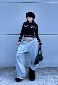 Pull noir court avec accents blancs, pantalon de survêtement gris oversize, chapeau en fourrure et petit sac à main noir. Ceinture perlée ajoutant du détail.