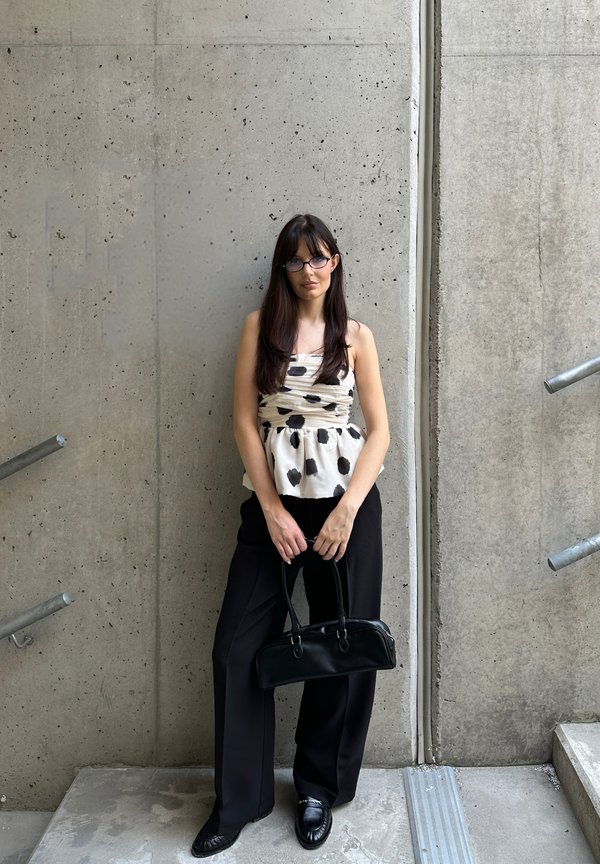 Top peplum com bolinhas pretas e brancas, com detalhe franzido, combinado com calças largas pretas e uma mala estruturada preta.