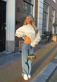 Sweat-shirt beige oversize avec texte "MULTIPLY", jean bleu taille haute et sac à main noir. Comprend des baskets blanches avec des accents roses.