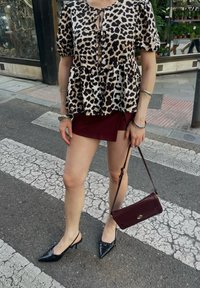 Bluză cu imprimeu leopard, cu mâneci scurte tip puff, fustă mini burgundă, pantofi slingback negri cu vârful ascuțit și o geantă mică de umăr burgundă.