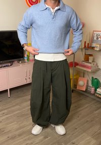 Lichtblauwe wollen pullover met kraag, wit ondershirt en olijfgroene wijde broekspijpen. Model draagt witte sneakers en staat binnen.