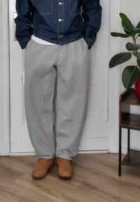Pantalones deportivos de color gris claro con una cinturilla elástica, combinados con botas de tobillo de ante marrón. Chaqueta de mezclilla sobre una camiseta blanca. Entorno interior.