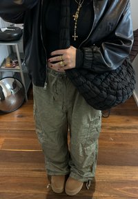 Μαύρο μπουφάν, εφαρμοστό μαύρο τοπ, ελαιόχρωμο cargo παντελόνι, μπεζ μπότες, υφασμένο μαύρο τσάντα, πολλαπλά χρυσά σταυρουδάκια σε στρώσεις, πολλά δαχτυλίδια.