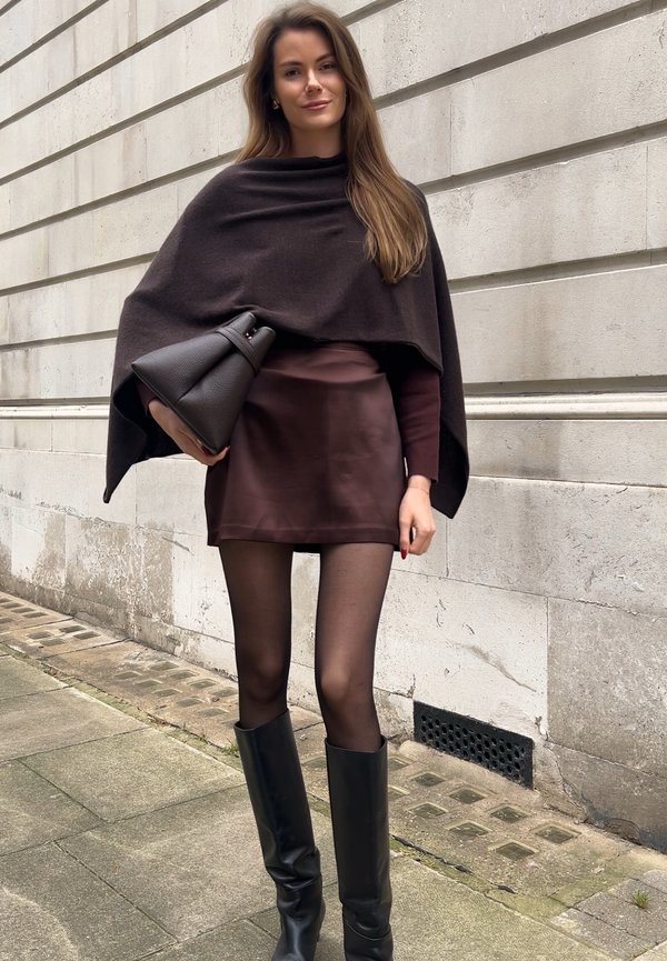 Poncho marrone su una maglietta bordeaux, abbinato a una mini gonna marrone, collant neri trasparenti e stivali neri al ginocchio. Accentuato da una borsa nera texturizzata.