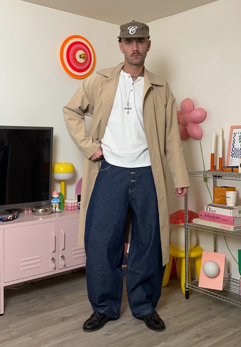 Bēša gara mētelis pār baltu kreklu, kopā ar pārlieliem zilajiem džinsa bikšu. Melni apavi un rūtainas cepure. Vienkārša sudraba ķēdes kaklarota.