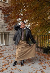 Svart skinnjakke, grønn genser, rutet slips og khakifarget skjørt. Sorte spisse ankelstøvler. Høstblader i bakgrunnen.