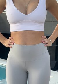 Brassière de sport rose clair avec un design à col en V, associée à des leggings gris clair taille haute avec un petit logo Nike sur la ceinture.