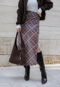 Saia xadrez em roxo e bege com uma abertura lateral, combinada com uma bolsa de camurça castanha e botas pretas de salto alto até ao joelho.