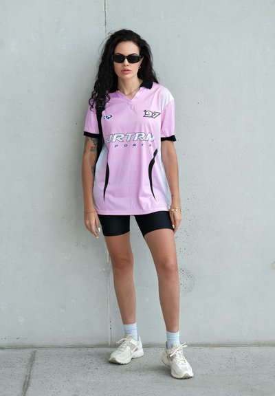 Camiseta deportiva rosa con detalles en negro y malla, combinada con pantalones cortos negros y zapatillas blancas. Independiente; sin características adicionales.