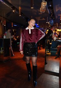 Top de manga larga de terciopelo granate con cuello blanco y tres rayas blancas, combinado con una minifalda negra de lentejuelas y botas negras altas con tacón.