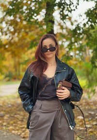 Melnas ādas jaka virs melnas mežģīņu camisole. Olīvzaļas platās bikses. Turēšana brūnā somiņā. Saulesbrilles papildina izskatu.