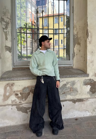 Sudadera de forro polar verde menta con cuello, combinada con pantalones de mezclilla negros de corte oversized. Detalles de llavero en los pantalones. Calzado en tonos neutros.