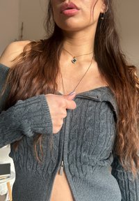 Grey knitted sweater with a cable pattern, featuring a front zip and an off-shoulder design. The texture looks soft and snug.