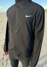 Must musta Nikes, millel on ees lukk, kõrge krae ja pikad varrukad. Omab väikest valget swooshi logo vasakul ülal rinnas.