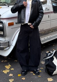 Fekete, bőszárú nadrág, fehér ing krémszínű dzseki alatt, és fekete bőrkabát. Fekete fapapucs díszítőelemekkel. Marhabőr táska.