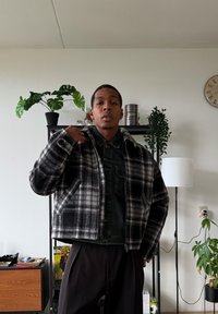 Veste en laine à carreaux noir et blanc avec une fermeture éclair à l'avant, un col, et des poches latérales, portée sur une chemise en denim foncé.