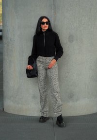 Μαύρο πλεκτό πουλόβερ με μπροστινό φερμουάρ και μακριά μανίκια, συνδυασμένο με γκρίζες παντελόνες με λεοπάρ σχέδιο. Μαύρα γυαλιά ηλίου και μαύρη τσάντα χειρός. Χοντρά μαύρα μποτάκια.