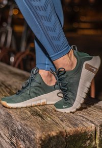 Zöld sportcipők textil felső résszel, gumitalppal, fűzővel és kontrasztos világosbarna kiegészítővel. Ráncolt dizájn részletek láthatók.