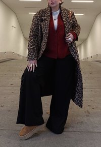 Παλτό λεοπάρ, κόκκινο υφασμάτινο καρό κορμάκι, μαύρο παντελόνι με φαρδιά ποδωμάκια, καφέ πλατφόρμες μπότες. Τα αξεσουάρ περιλαμβάνουν στρώσεις δακτυλίδια και βραχιόλια.