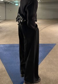 Čierne nadmerné nohavice s rovno strihom, doplnené čiernou crossbody taškou s detailmi na pracke. Hladká látka s minimálnou textúrou.