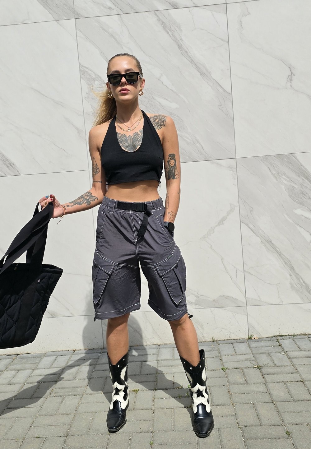 Μαύρο κοντό μπλουζάκι, γκρι cargo σορτς με πολλαπλές τσέπες, μαύρα και λευκά καουμπόικα μποτάκια με σχέδιο αστέρια και μια μαύρη τσάντα χειρός.