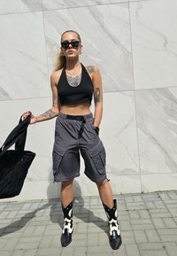 Μαύρο κοντό μπλουζάκι, γκρι cargo σορτς με πολλαπλές τσέπες, μαύρα και λευκά καουμπόικα μποτάκια με σχέδιο αστέρια και μια μαύρη τσάντα χειρός.