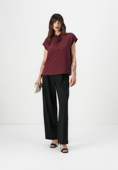 Top burdeos con un lazo en el cuello y mangas cortas, combinado con pantalones negros holgados. Presenta una tela suave y un diseño minimalista. Acentuado con sandalias de tacón.