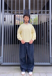 Sweatshirt amarelo claro com design texturizado, combinado com jeans escuros de corte largo. O calçado é branco com sola castanha.