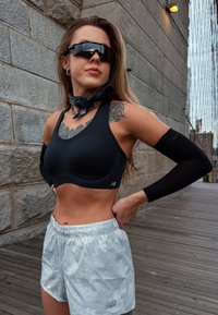 Čierna športová podprsenka s výstrihom do U a logom, v kombinácii so striebornými krátkymi nohavicami s potlačou a čiernymi rukávmi na ruky. Doplnky zahŕňajú slnečné okuliare a šatku.